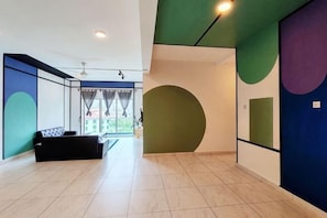 A spacious room with a large window, a black sofa, and a green accent wall.