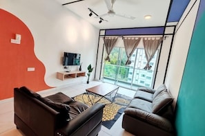 A modern living room with a sofa set, a coffee table, a flat-screen TV, and a large window with curtains. - Icolor Home & Stay CH4 (Tanah Rata)