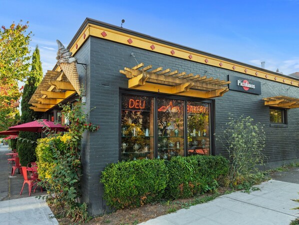 A bakery with a neon sign, outdoor seating, and a brick facade.