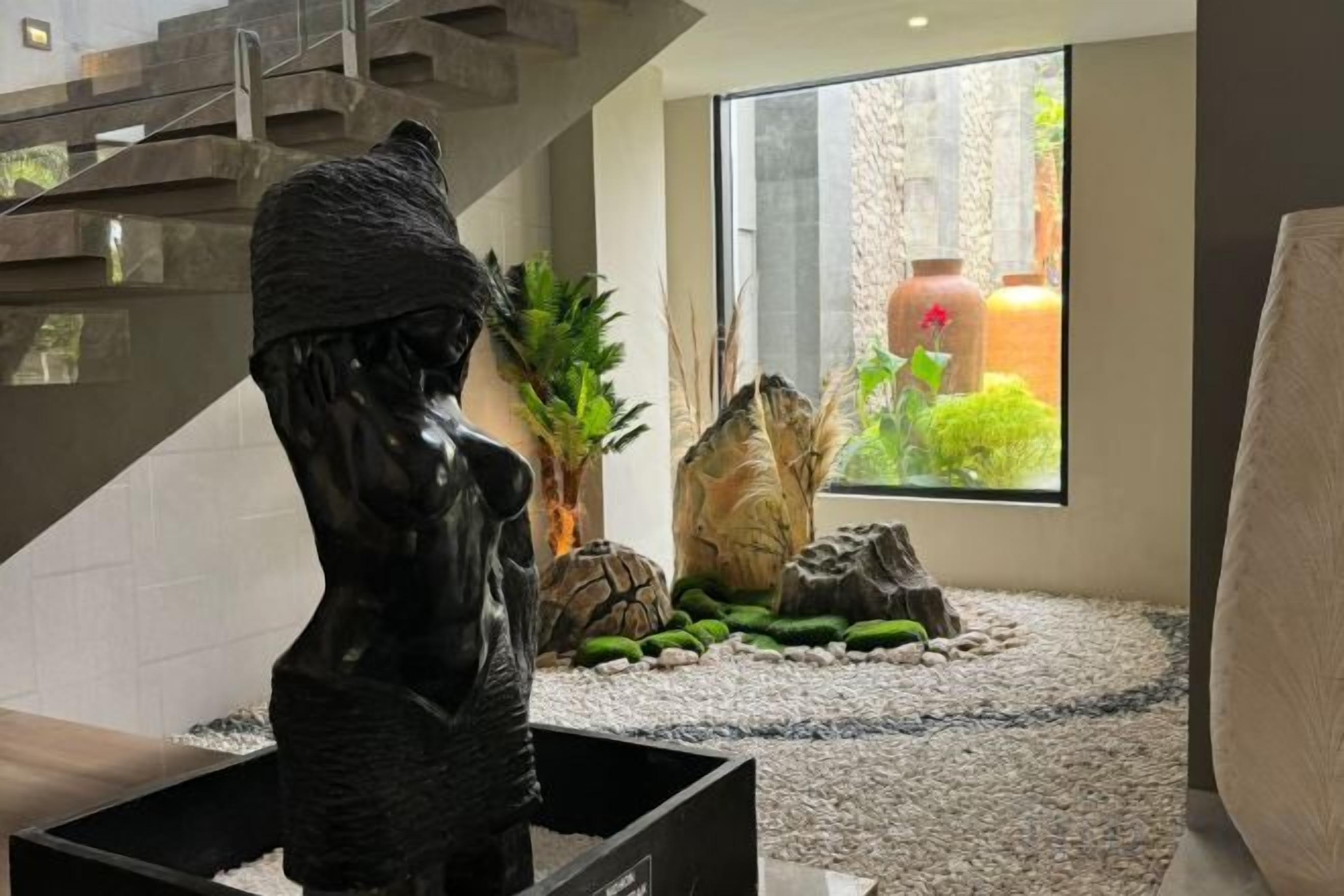 Eine Skulptur in einem Raum mit Blick auf einen Garten, eine Treppe und ein großes Fenster.
