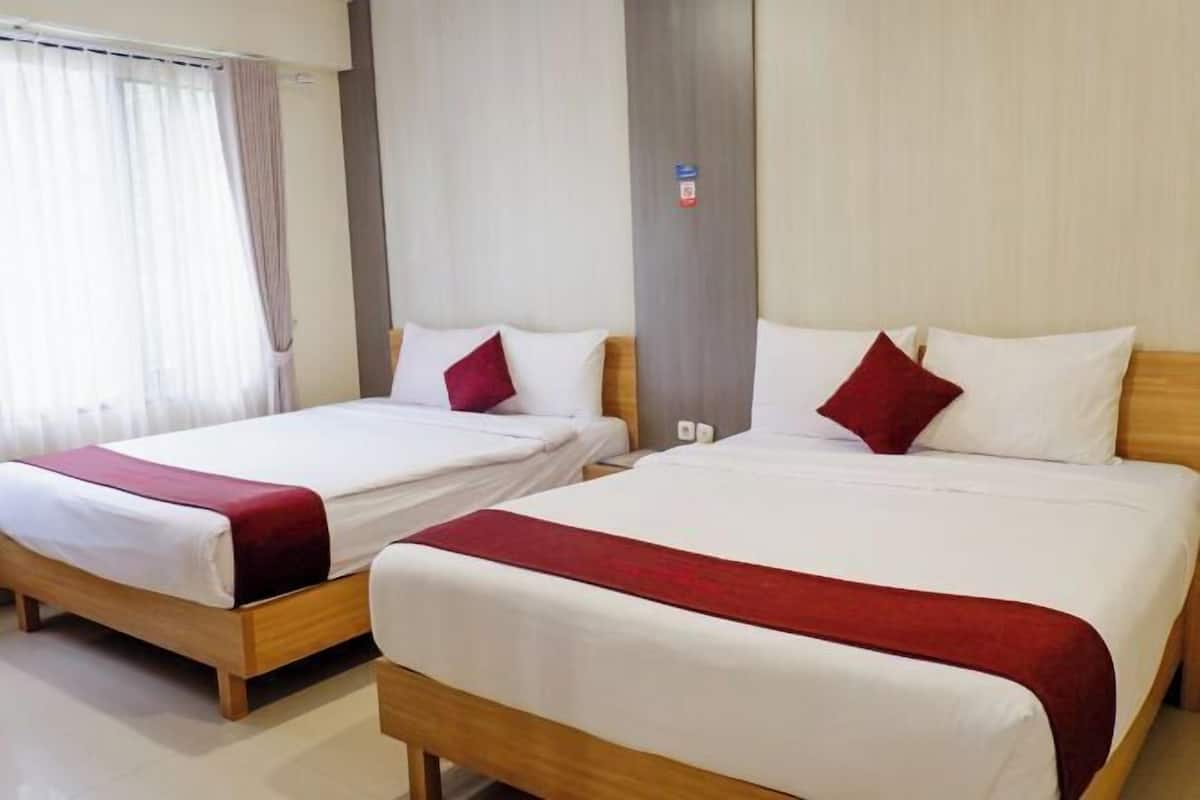 Due letti matrimoniali con struttura in legno e biancheria bianca, cuscini rossi e una coperta rossa su ogni letto.