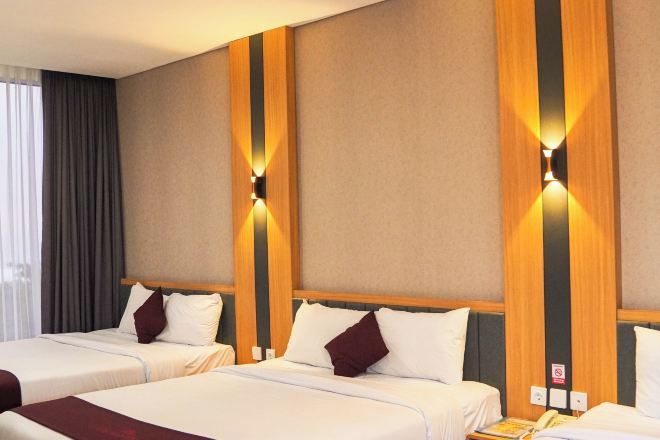 A hotel room with three beds, a wooden accent wall, and a window with curtains.