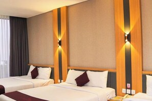 A hotel room with three beds, a wooden accent wall, and a window with curtains. - Long Beach Hotel Pangandaran (Pangandaran)