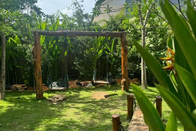 A wooden swing set in a lush garden with a clear sky.