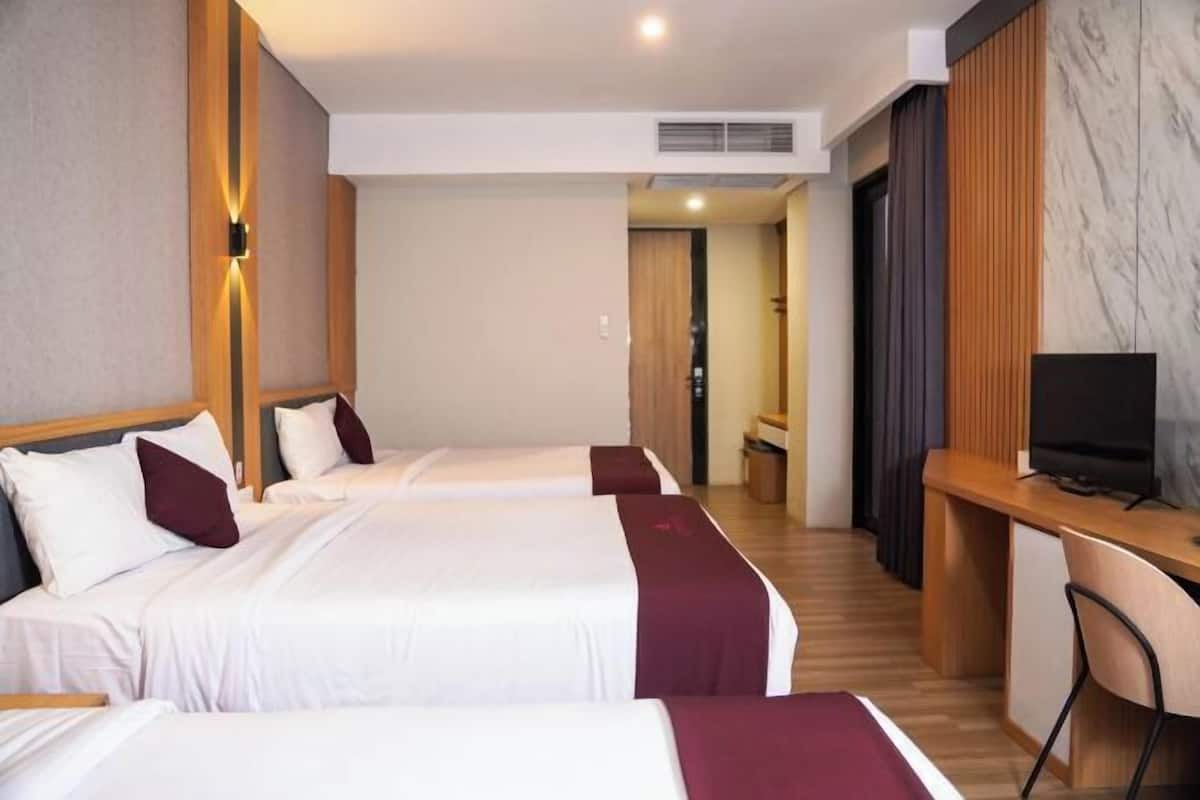 Una camera d'albergo con tre letti, una scrivania e una televisione.