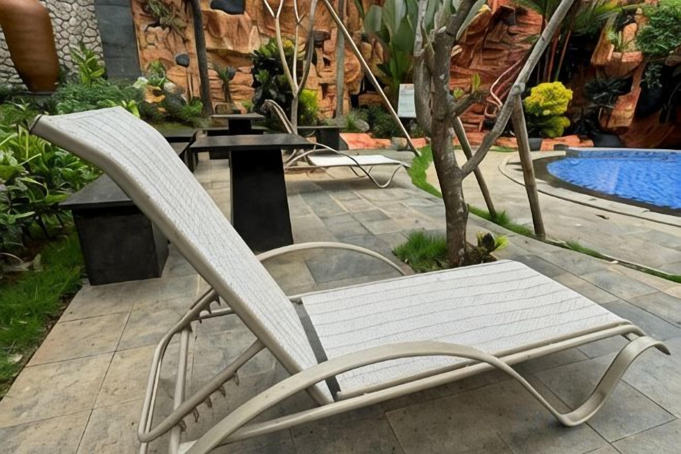 Una silla de salón en un entorno exterior con una piscina y un muro decorativo al fondo.