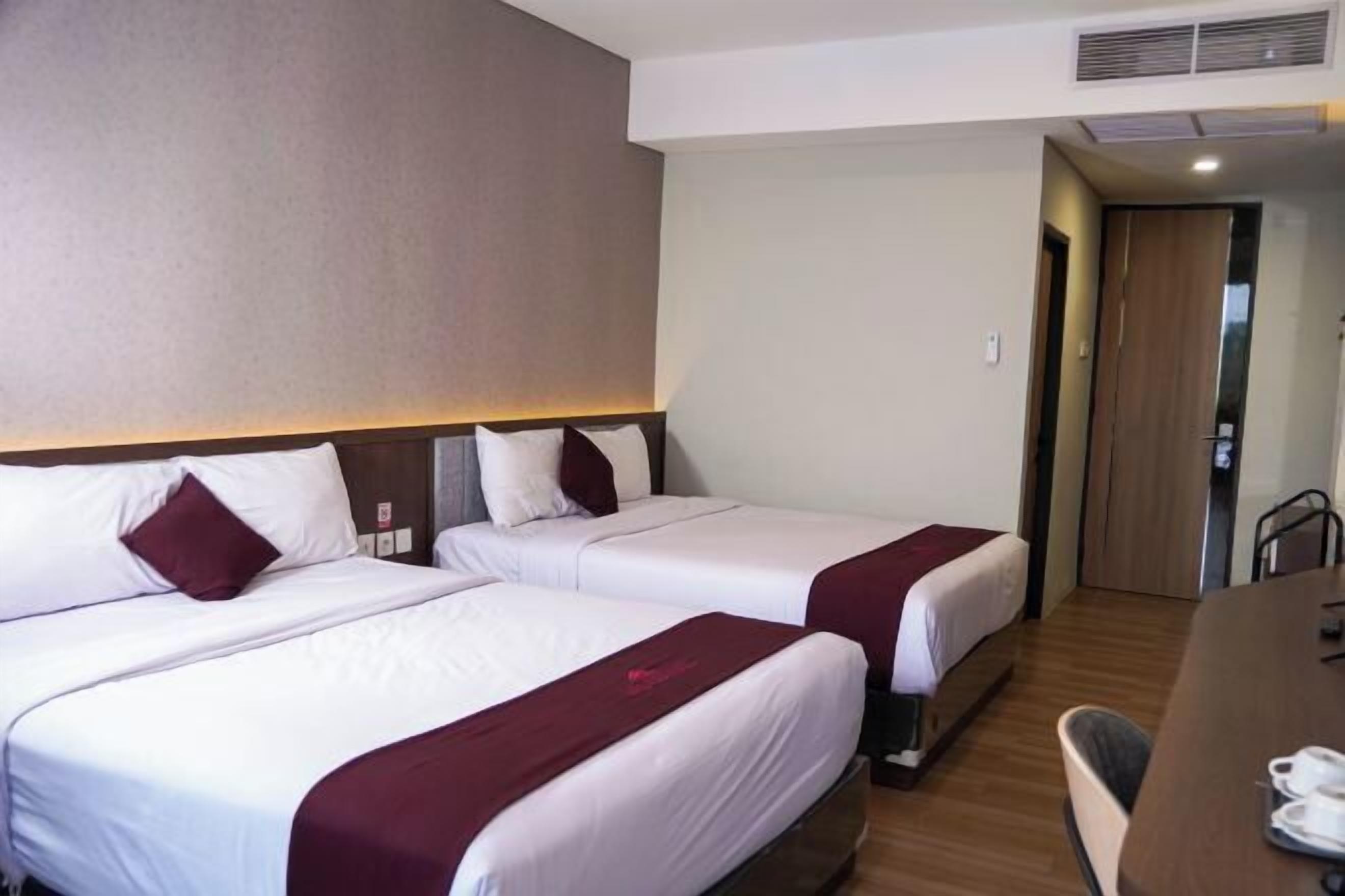 A hotel room with two beds, a wooden desk, and a door leading to another room.