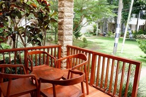 A wooden deck with a table and chairs, surrounded by greenery and a stone pillar. - Long Beach Hotel Pangandaran (Pangandaran)