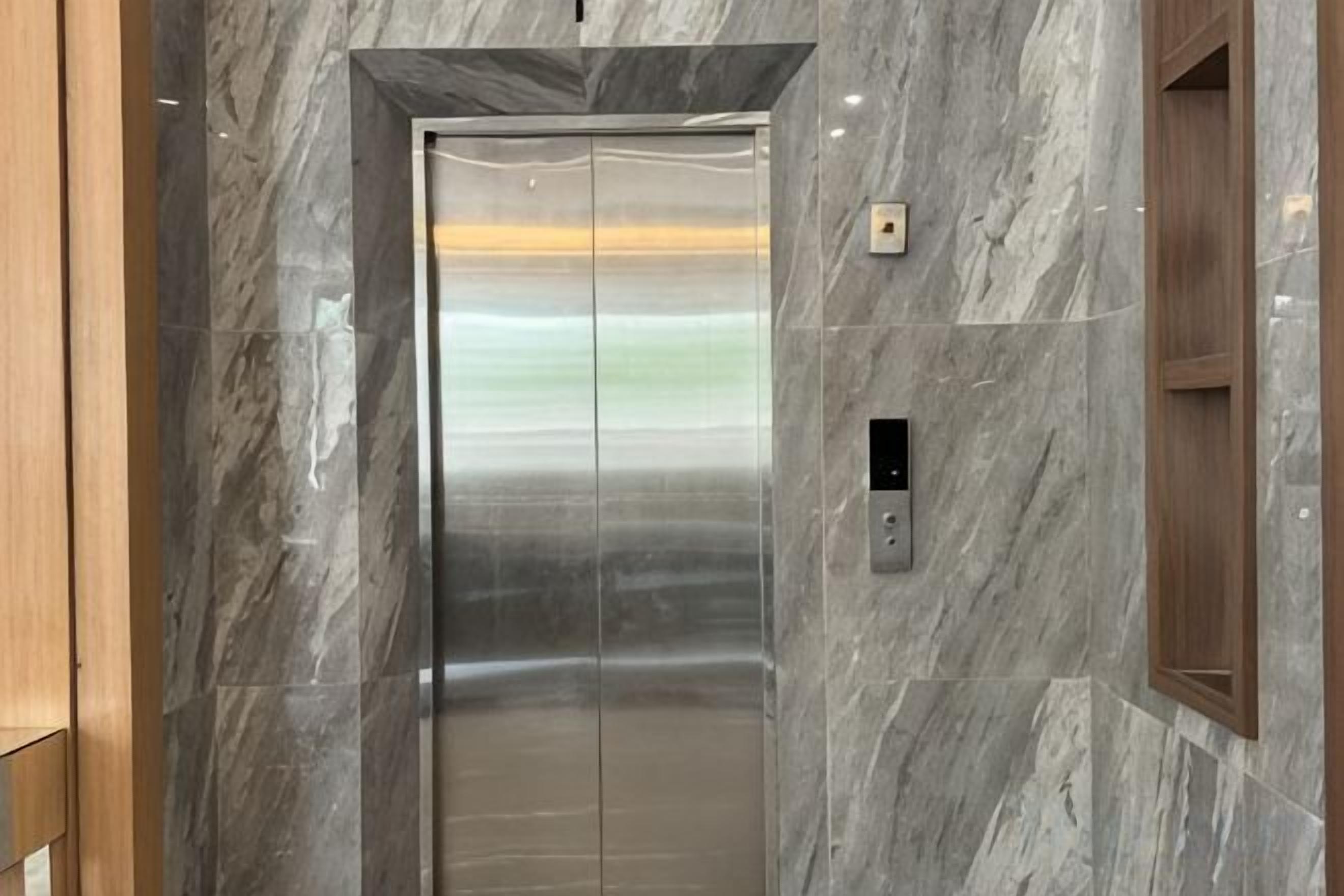 An elevator with a metallic finish, a control panel, and a marble wall.
