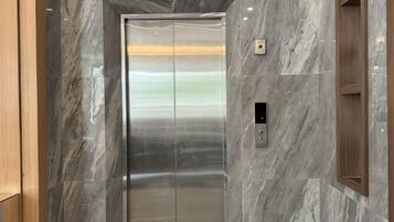 An elevator with a metallic finish, a control panel, and a marble wall.