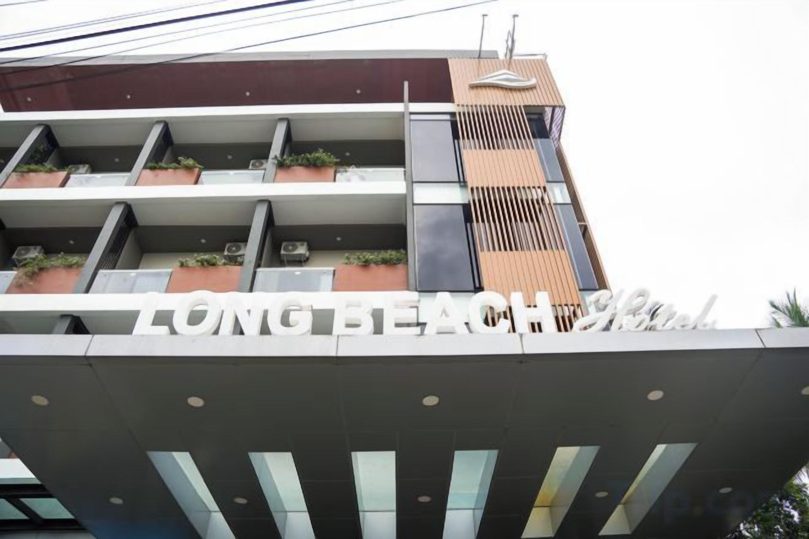 Un edificio con un letrero que dice 'LONG BEACH Hotel'. Cuenta con varios balcones con plantas y un diseño arquitectónico moderno.