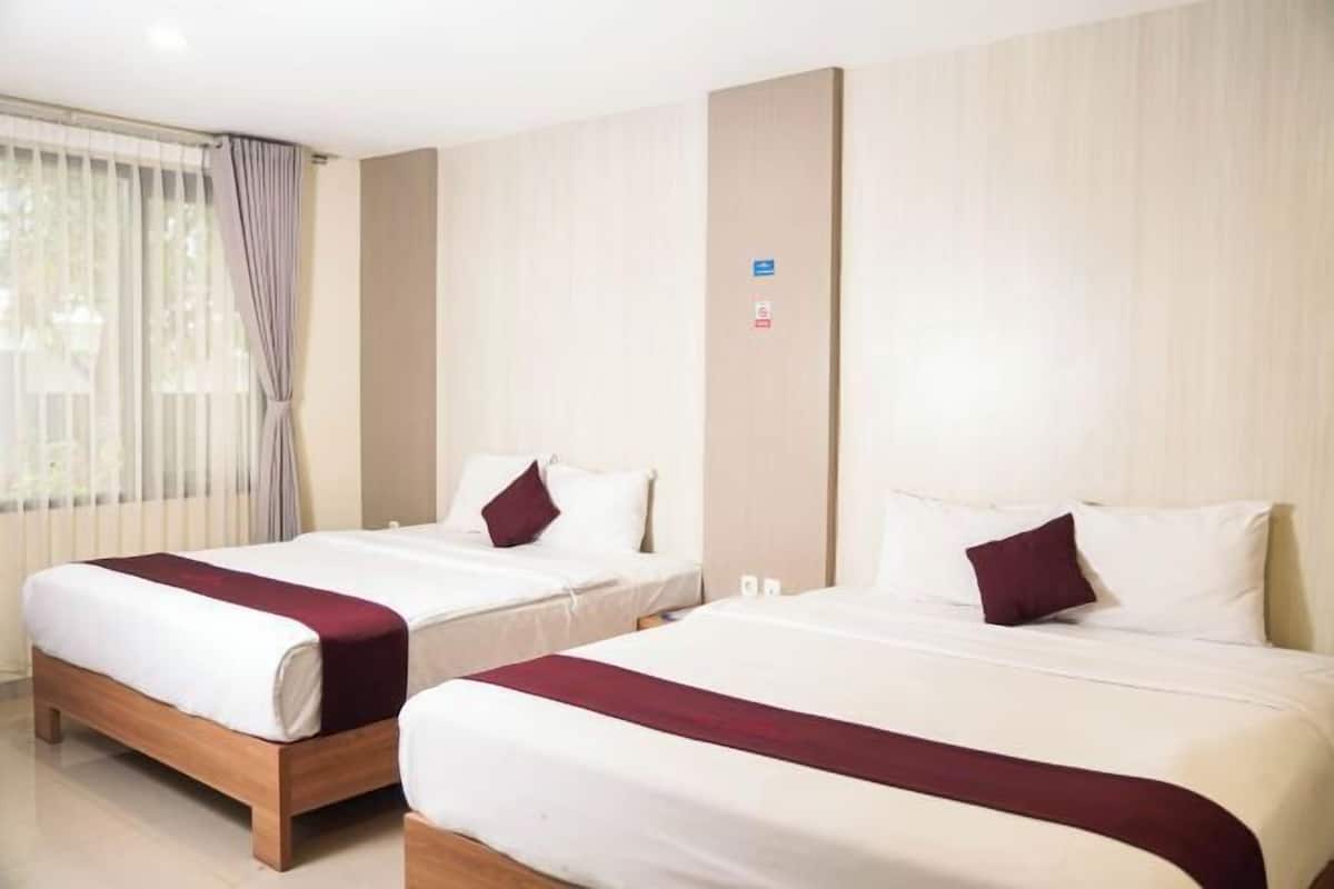 Due letti singoli con biancheria da letto bianca e dettagli color borgogna, una testiera in legno, una parete di colore chiaro e una finestra con tende.