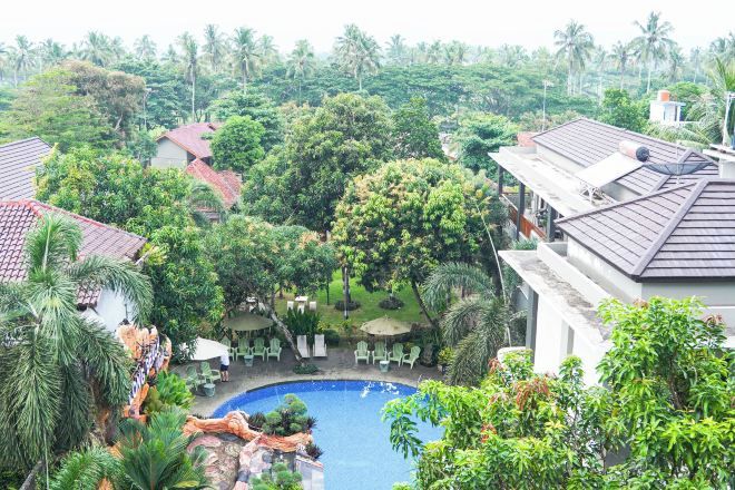 A pool surrounded by lush greenery and palm trees, with outdoor seating and a view of the surrounding landscape.