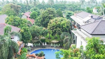 A pool surrounded by lush greenery and palm trees, with outdoor seating and a view of the surrounding landscape.