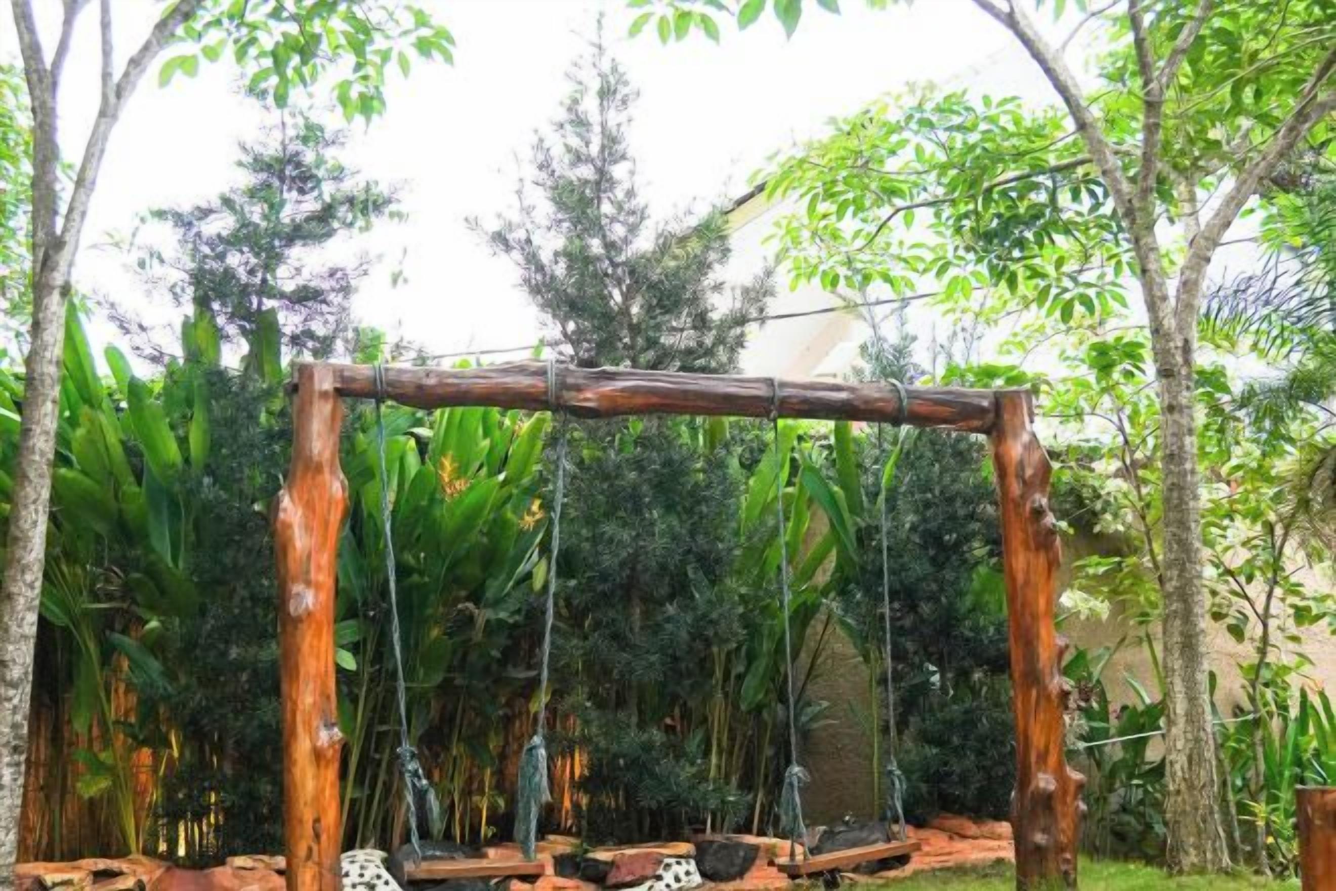 A wooden swing set in a garden with dense foliage in the background.