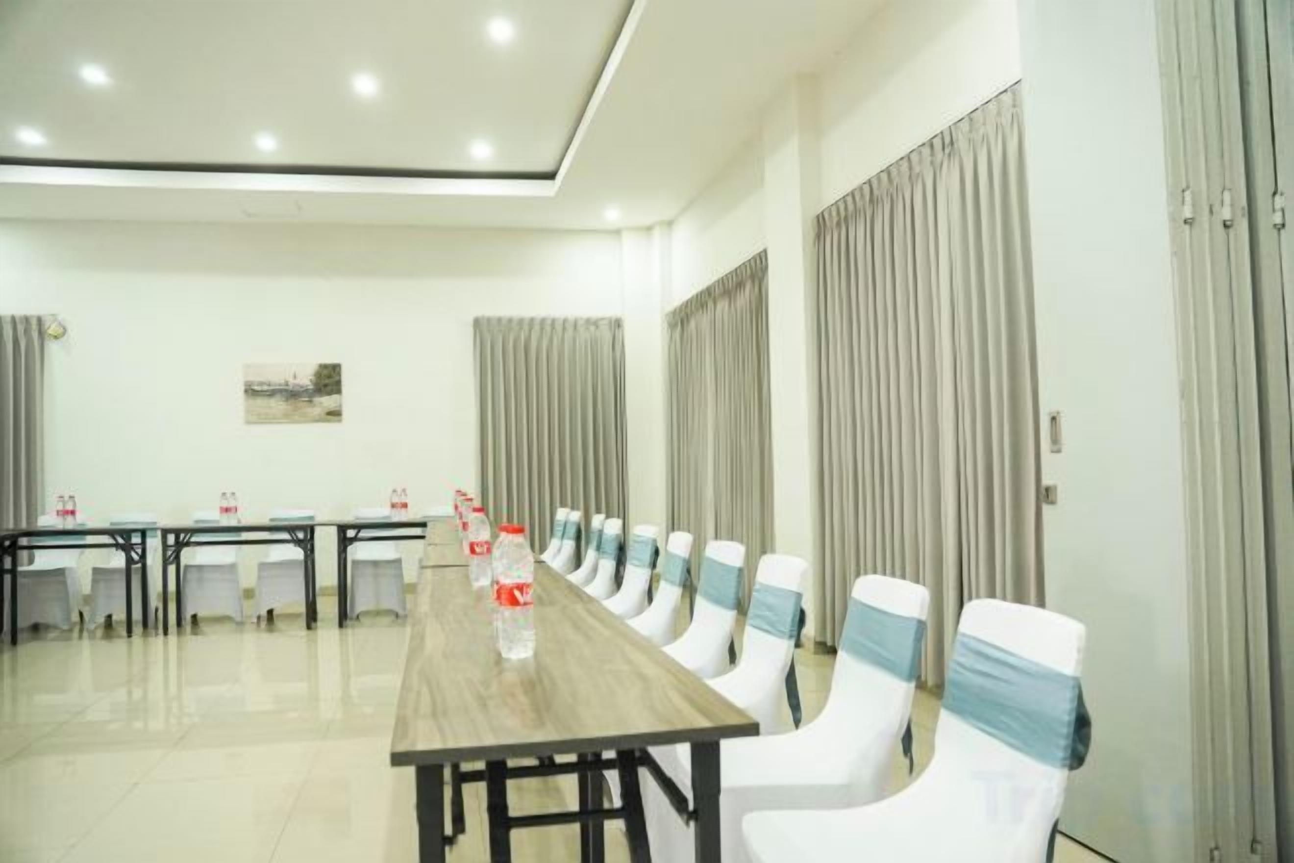A conference room with a long table and chairs, a painting on the wall, and curtains on the windows.