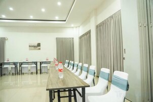 Un salón de conferencias con una larga mesa y sillas, un cuadro en la pared y cortinas en las ventanas.