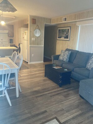 A living room with a sofa, a coffee table, and a dining area with chairs and a table.