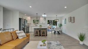 A modern kitchen with a central island, wooden stools, and pendant lighting.