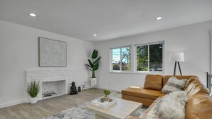 A modern living room with a white brick fireplace, a large window, and a brown leather sofa.