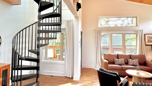A spacious living area with a wooden floor, a spiral staircase, a brown sofa with patterned cushions, and a round wooden coffee table. - Minutes to Dollywood, New, Sleeps 6 (Pigeon Forge)