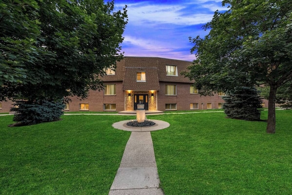 A two-story building with a central entrance, surrounded by a well-maintained lawn and trees.