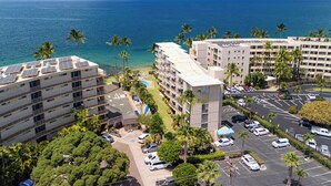 A hotel with multiple floors, a parking lot, and a view of the ocean. - Kamaole Nalu 506 - Ocean Front (Kihei)