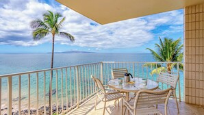 A balcony with a view of the ocean, a round table with chairs, and a railing. - Kamaole Nalu 506 - Ocean Front (Kihei)