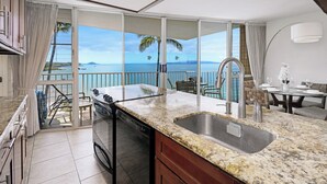 A modern kitchen with a large island, a dishwasher, and a view of the ocean.