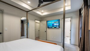 Ein Hotelzimmer mit einem Bett, einem an der Wand befestigten Fernseher und einer Tür zu einem weiteren Zimmer.