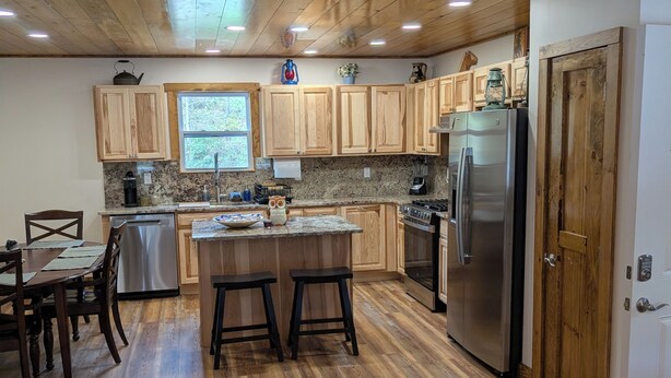 A kitchen with wooden cabinets, a central island with stools, stainless steel appliances, and a window providing natural light.