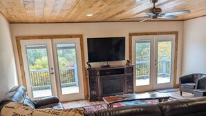 A living room with a large black leather couch, a wooden ceiling, a fireplace, and a television.