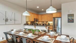 Una cocina moderna con armarios de madera, electrodomésticos de acero inoxidable y un comedor preparado para seis personas con una mesa de madera grande.