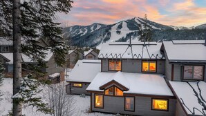 Una casa de varios pisos con tejados nevados y ventanas, rodeada de árboles y montañas.