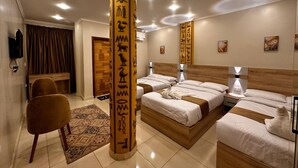 A hotel room with a large bed, two smaller beds, a desk, and a chair. - Pyramids On The Spot Inn (Giza)