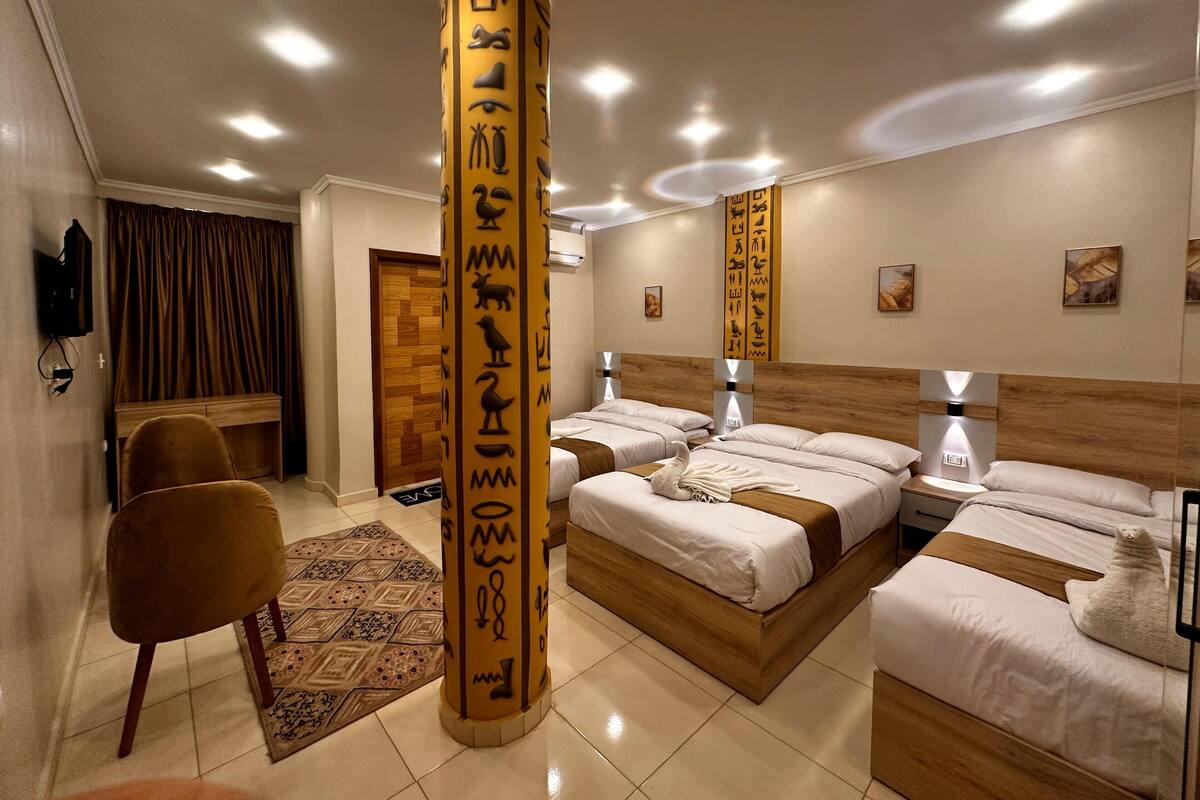 Quarto de hotel com uma cama grande, duas camas menores, uma escrivaninha e uma cadeira.