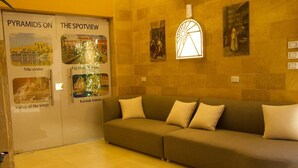 A room with a beige sofa, a wall-mounted light fixture, and posters about Egypt. - Pyramids On The Spot Inn (Giza)