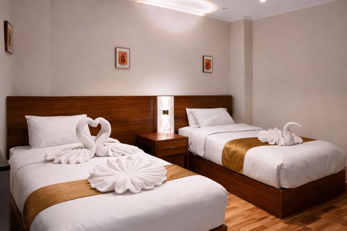 Quarto de hotel com duas camas, cabeceiras de madeira, roupa de cama branca e piso de madeira.