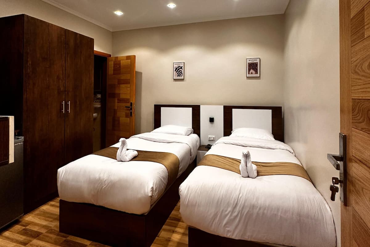 Quarto de hotel com duas camas, piso de madeira e um guarda-roupa.