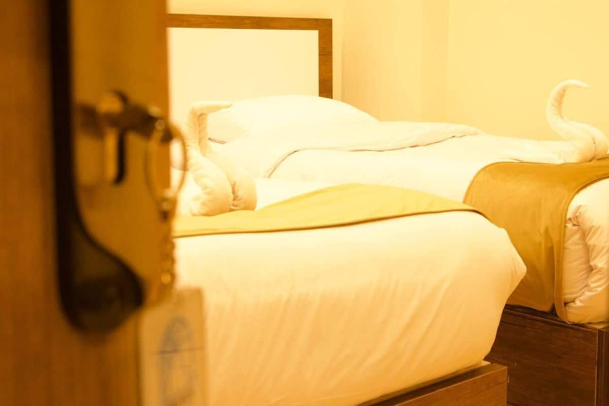 Quarto de hotel com uma cama, cabeceira de madeira e porta com maçaneta.