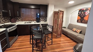 A compact kitchen with a stove, sink, and a dining area with chairs. A sofa and a decorative panel are in the living area. - Your private space in an excellent location (Juárez)