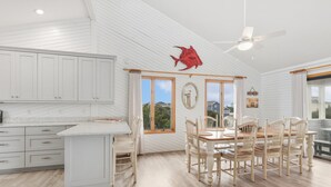 A modern kitchen with white cabinetry, a dining area with wooden chairs, and a ceiling fan. - Saltwater Pool, Bar & Ocean Views – Duck OBX (Duck)
