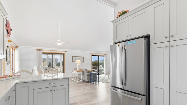A modern kitchen with grey cabinets, a stainless steel refrigerator, and a dining area with a table and chairs. - Saltwater Pool, Bar & Ocean Views – Duck OBX (Duck)