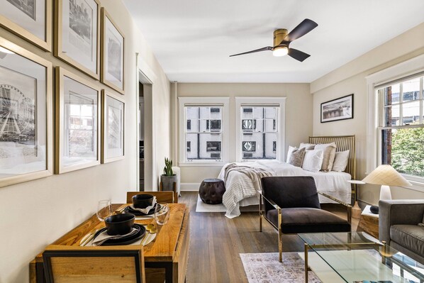 A bedroom with a bed, a desk with a chair, a sofa, and a ceiling fan.