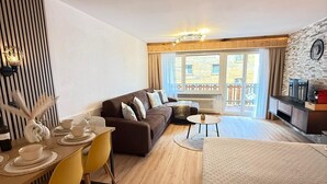Une chambre d’hôtel moderne avec un plancher en bois, un canapé, une table à manger avec des chaises jaunes, une petite table ronde et un lit.