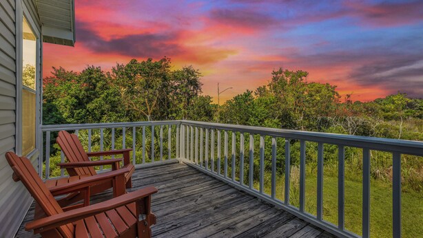 A wooden deck with two Adirondack chairs, a railing, and a view of trees and a sunset. - Beach Days & Fire Nights! Family 3BR Duplex Just Steps from the Sand! (Gulf Shores)