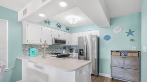 A kitchen with white cabinets, a stainless steel refrigerator, a microwave, and a blue coffee maker. - Beach Days & Fire Nights! Family 3BR Duplex Just Steps from the Sand! (Gulf Shores)