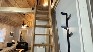 A wooden interior with a central wooden staircase, a white wall, and a sofa in the foreground.