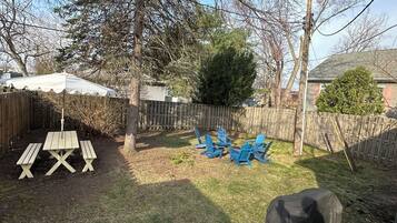 Un patio trasero con una mesa de picnic, sillas de jardín azules, una parrilla y una cerca de madera.
