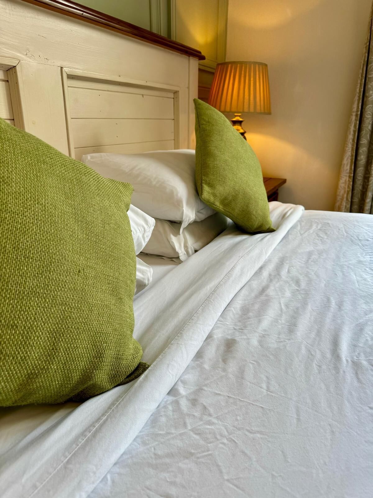 Een net opgemaakt bed met witte lakens en twee groene kussens.